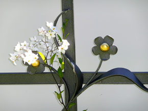 Mit Blumen umranktes Kreuz aus Metall in Detailansicht